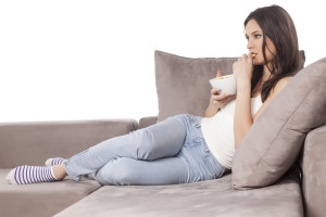 beautiful young woman sitting on the couch and eating chips